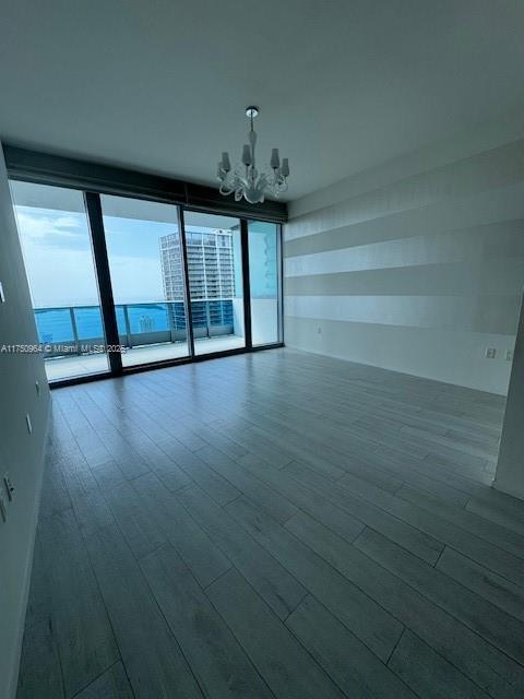 spare room with a chandelier, dark wood-style flooring, and a wall of windows