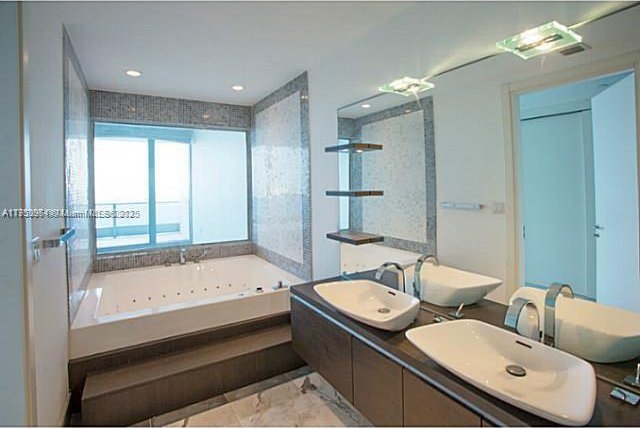 bathroom featuring recessed lighting, a sink, a jetted tub, and double vanity