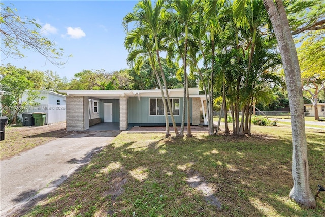 ranch-style home with a front yard, a carport, brick siding, fence, and aphalt driveway