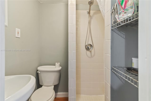 full bathroom with baseboards, a tile shower, and toilet