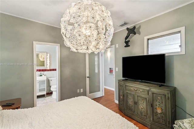 bedroom featuring crown molding, visible vents, wood finished floors, baseboards, and ensuite bathroom