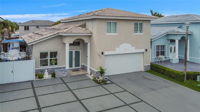 mediterranean / spanish-style home featuring a tile roof, fence, stone siding, french doors, and stucco siding