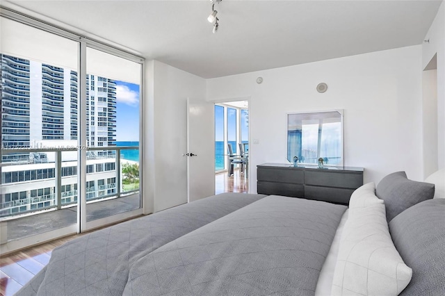 bedroom featuring wood finished floors, a water view, a wall of windows, rail lighting, and access to outside