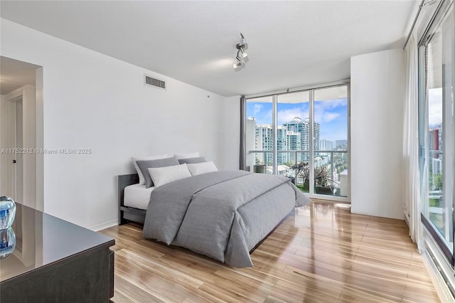 bedroom with light wood-style flooring, a city view, visible vents, access to outside, and track lighting