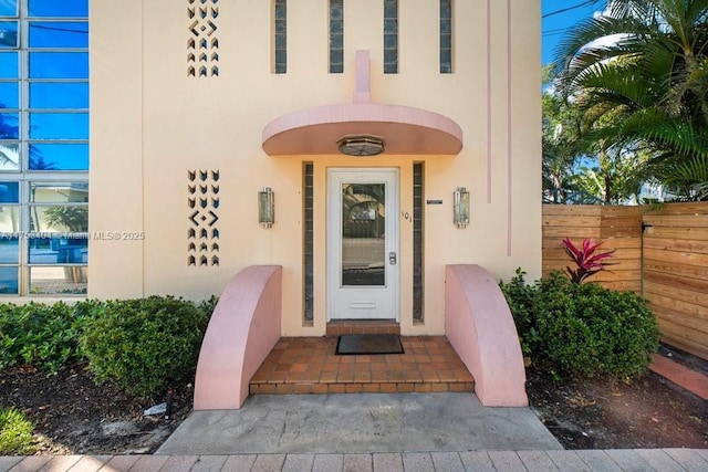 doorway to property featuring fence and stucco siding