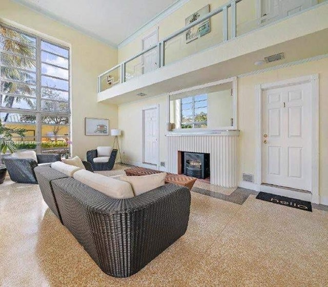 living area featuring speckled floor, a high ceiling, a fireplace, visible vents, and ornamental molding