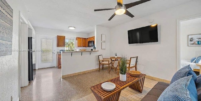 living area featuring light speckled floor, a textured ceiling, a ceiling fan, and baseboards