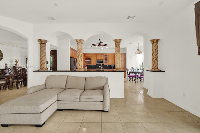 living area with ornate columns, light tile patterned floors, visible vents, and a notable chandelier