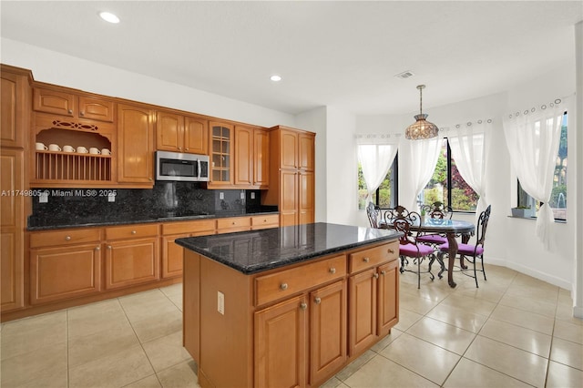 kitchen featuring light tile patterned floors, tasteful backsplash, stainless steel microwave, and brown cabinetry