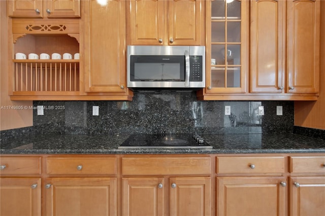 kitchen featuring glass insert cabinets, stainless steel microwave, backsplash, and black electric cooktop