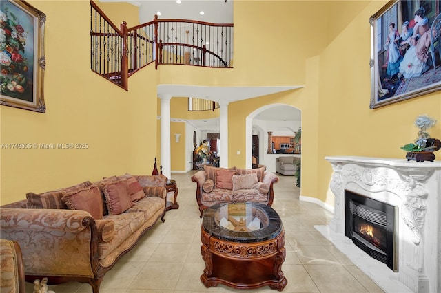 living room with a fireplace with flush hearth, arched walkways, a towering ceiling, and tile patterned floors