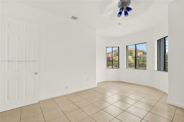 empty room with light tile patterned floors, a ceiling fan, visible vents, and baseboards