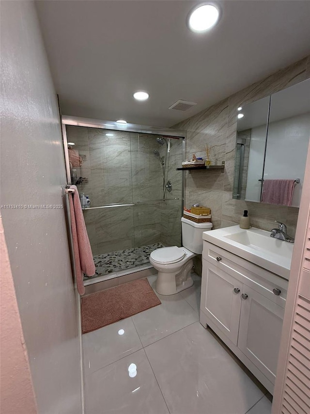 bathroom with tile walls, visible vents, toilet, a shower stall, and vanity