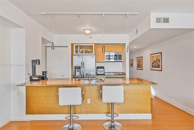 kitchen featuring light wood finished floors, stainless steel appliances, visible vents, a sink, and a peninsula