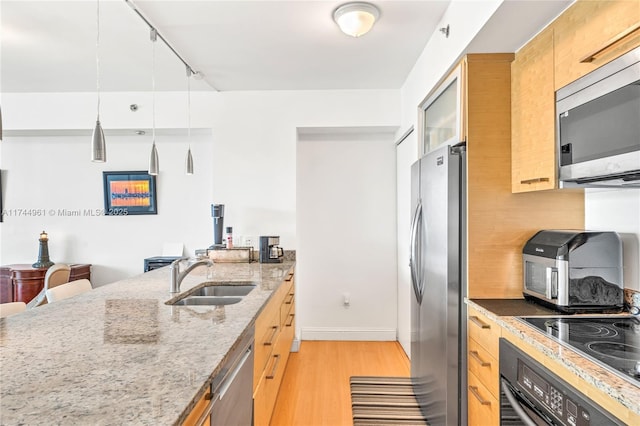 kitchen with light wood-style flooring, a sink, appliances with stainless steel finishes, light stone countertops, and decorative light fixtures