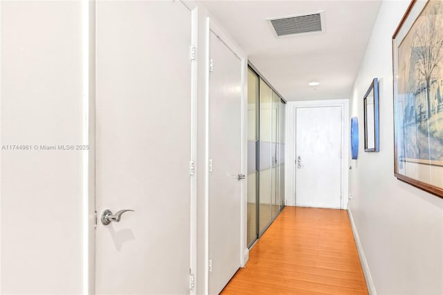 corridor with light wood finished floors, visible vents, and baseboards