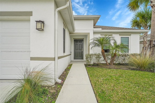 view of exterior entry with a garage, a yard, and stucco siding