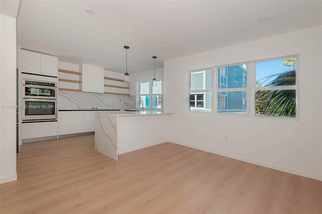 kitchen with light wood-style flooring, stainless steel double oven, white cabinets, and backsplash