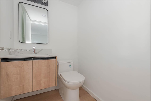 half bathroom with wood finished floors, vanity, toilet, and baseboards