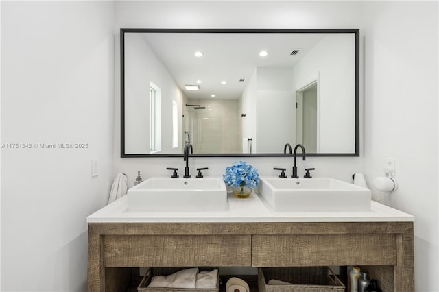 bathroom featuring a tile shower, double vanity, a sink, and visible vents