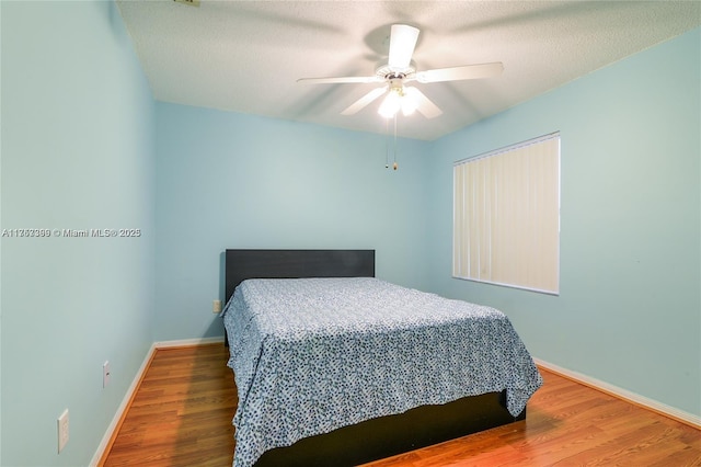 bedroom featuring ceiling fan, a textured ceiling, baseboards, and wood finished floors