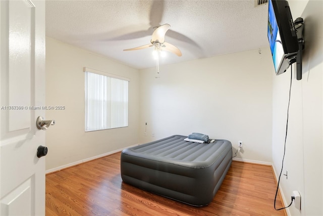 interior space with a ceiling fan, a textured ceiling, baseboards, and wood finished floors