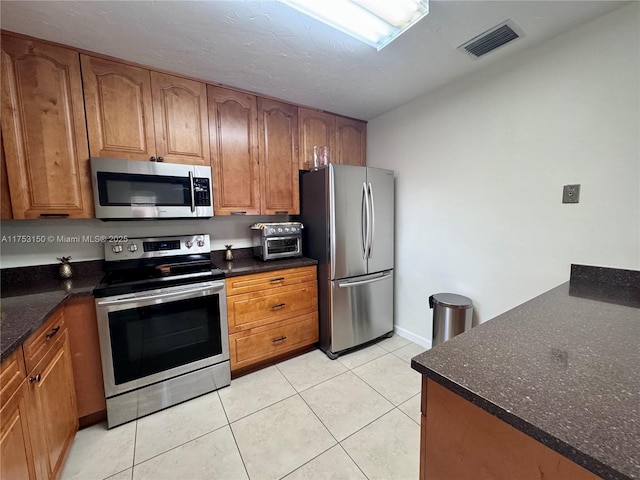 kitchen with stainless steel appliances, brown cabinets, visible vents, and light tile patterned floors