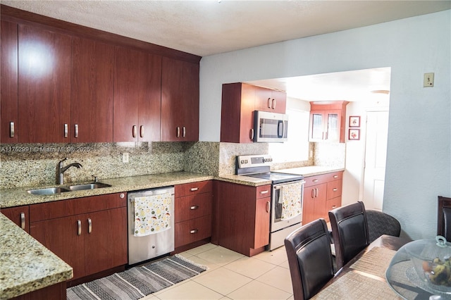 kitchen with light tile patterned floors, tasteful backsplash, light stone counters, stainless steel appliances, and a sink