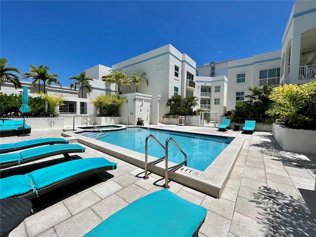 community pool with a patio area, fence, and a hot tub