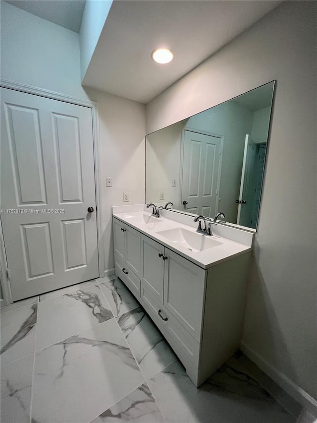 bathroom featuring marble finish floor, a sink, baseboards, and double vanity