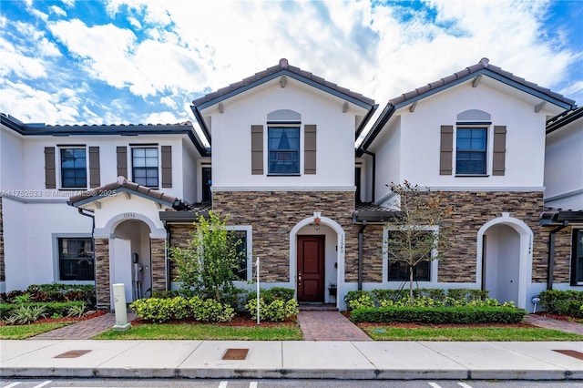 mediterranean / spanish home featuring stone siding, a tiled roof, and stucco siding