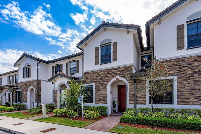 mediterranean / spanish-style house featuring stone siding, a tile roof, and stucco siding