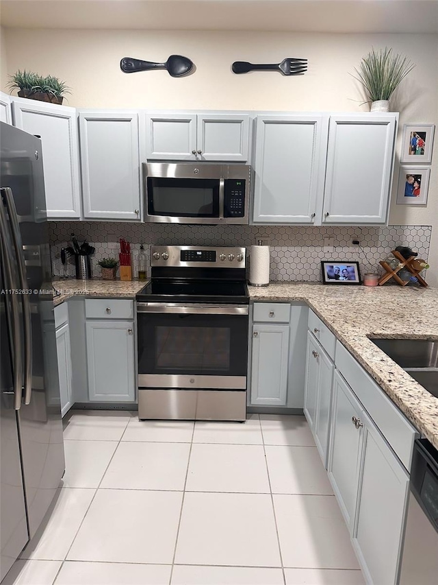 kitchen featuring stainless steel appliances, light stone countertops, decorative backsplash, and light tile patterned floors