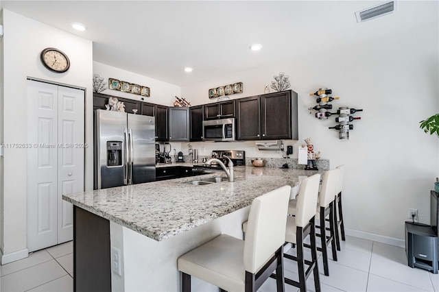 kitchen with stainless steel appliances, a peninsula, a sink, visible vents, and a kitchen breakfast bar