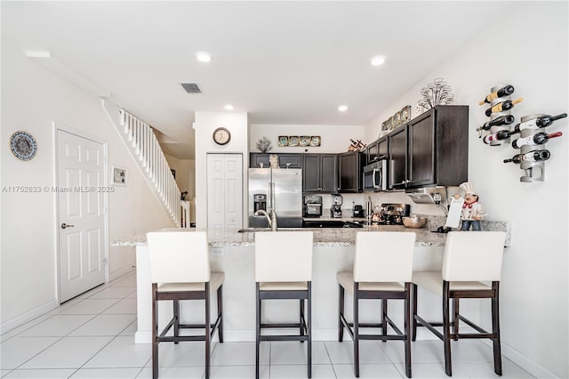 kitchen featuring light stone counters, visible vents, appliances with stainless steel finishes, a peninsula, and a kitchen bar