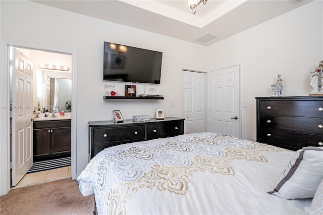 bedroom with light carpet, light tile patterned floors, visible vents, ensuite bathroom, and a closet