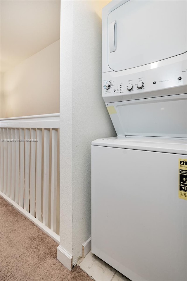 clothes washing area with carpet floors, laundry area, baseboards, and stacked washing maching and dryer