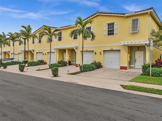 townhome / multi-family property with a garage, driveway, a tiled roof, and stucco siding