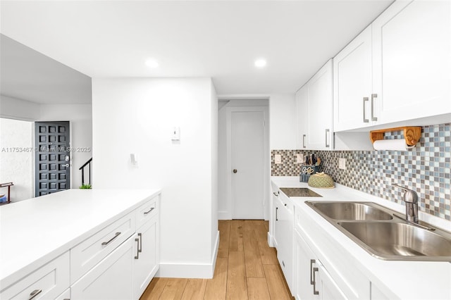 kitchen with a sink, white cabinetry, light countertops, decorative backsplash, and light wood finished floors