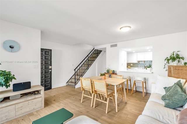 dining space featuring light wood-type flooring, stairs, and visible vents