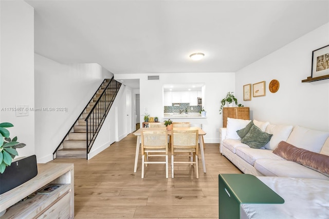 living room with stairs, light wood finished floors, visible vents, and baseboards