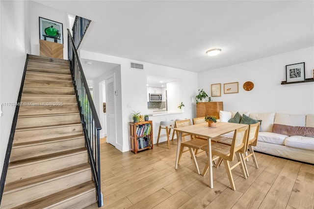 dining room featuring light wood-style flooring, stairs, and visible vents