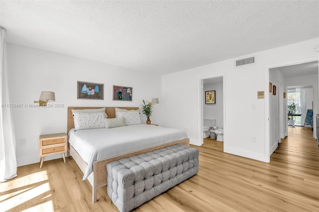 bedroom featuring a textured ceiling, baseboards, visible vents, and light wood-style floors