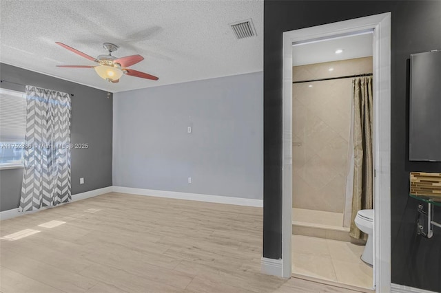 unfurnished bedroom featuring visible vents, a textured ceiling, ensuite bath, wood finished floors, and baseboards