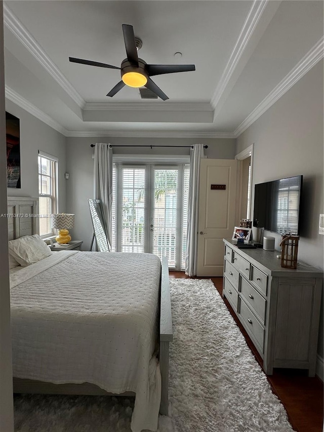 bedroom with access to exterior, a tray ceiling, dark wood finished floors, and a ceiling fan