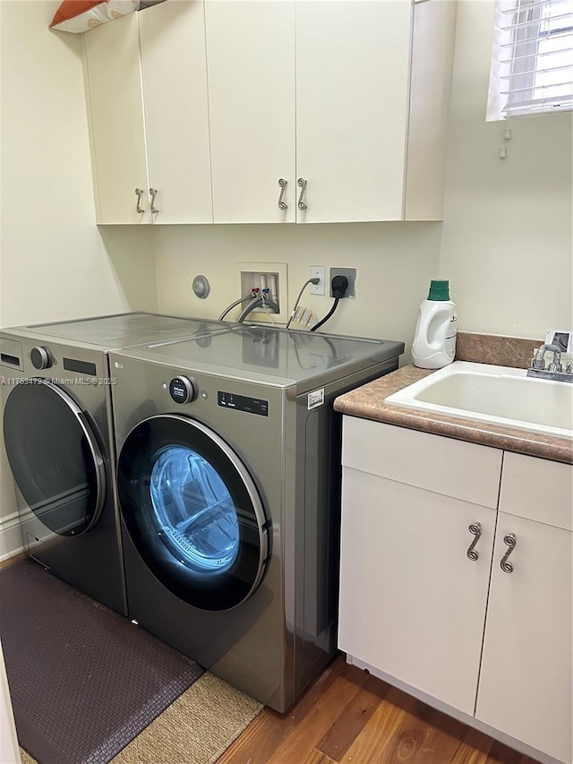 clothes washing area featuring cabinet space, independent washer and dryer, a sink, and wood finished floors