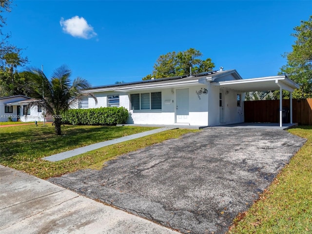 single story home with stucco siding, a front yard, roof mounted solar panels, a carport, and driveway