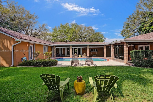 back of property featuring an outdoor pool, a lawn, a patio, a tile roof, and stucco siding