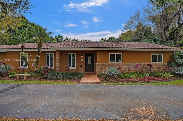 ranch-style house with brick siding, a tile roof, and stucco siding