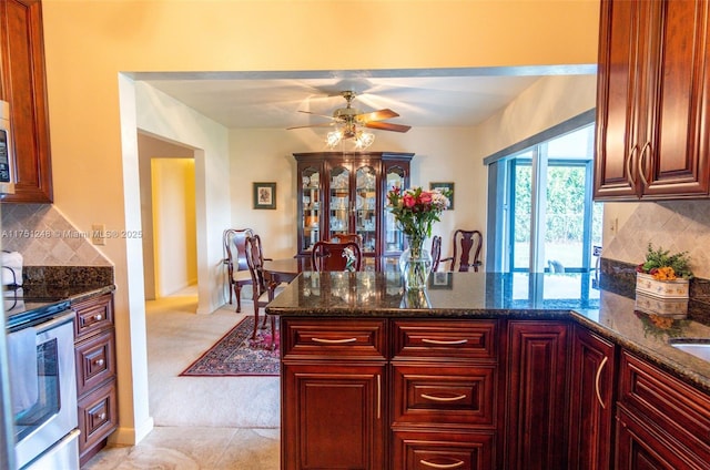 kitchen featuring dark stone counters, a peninsula, appliances with stainless steel finishes, and decorative backsplash